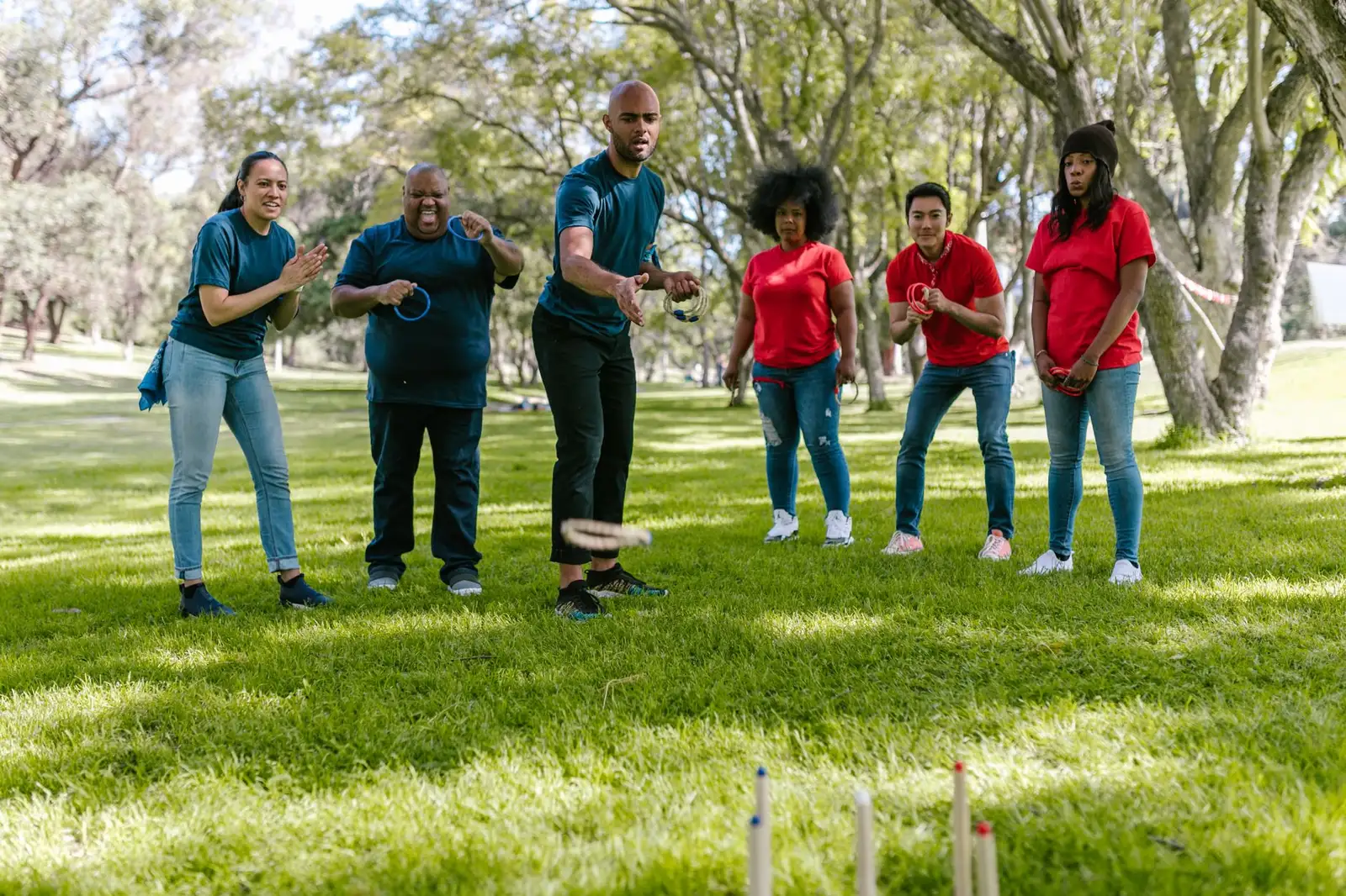 A diverse group enjoying a team building ring toss game outdoors in a sunny park.