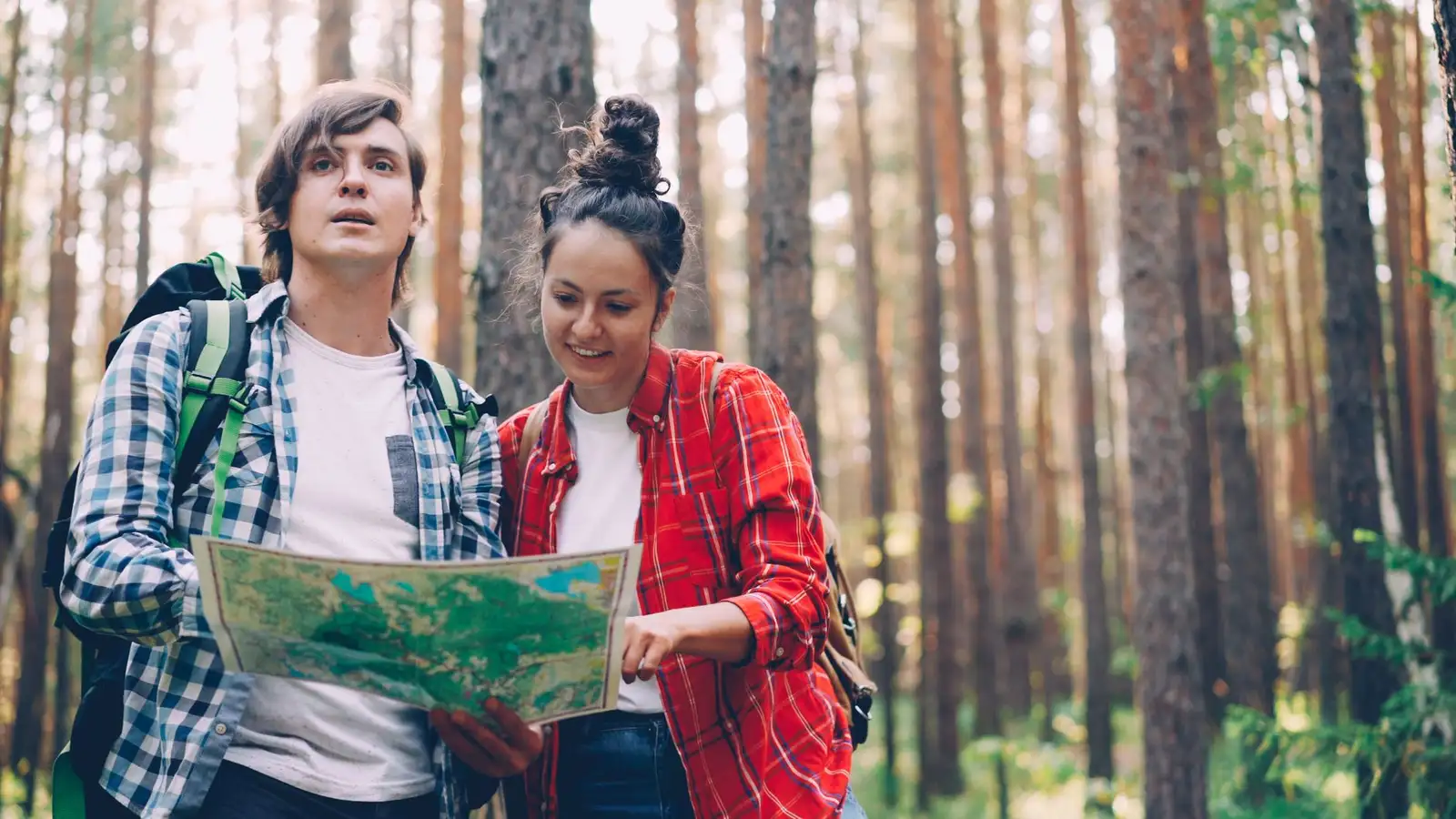 Two young adults hiking and reading a map in a dense forest.