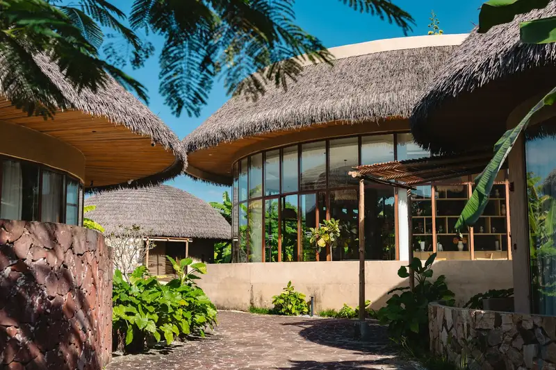 Charming tropical resort architecture with lush greenery and thatched roofs under a clear blue sky.