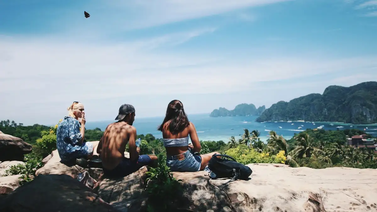 topless man sitting between two persons near body of water